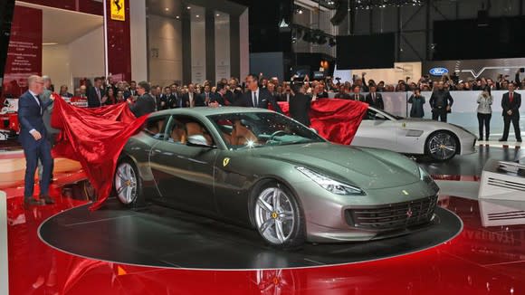 Someone pulling the cover off a Ferrari GTC4Lusso on a showroom floor.