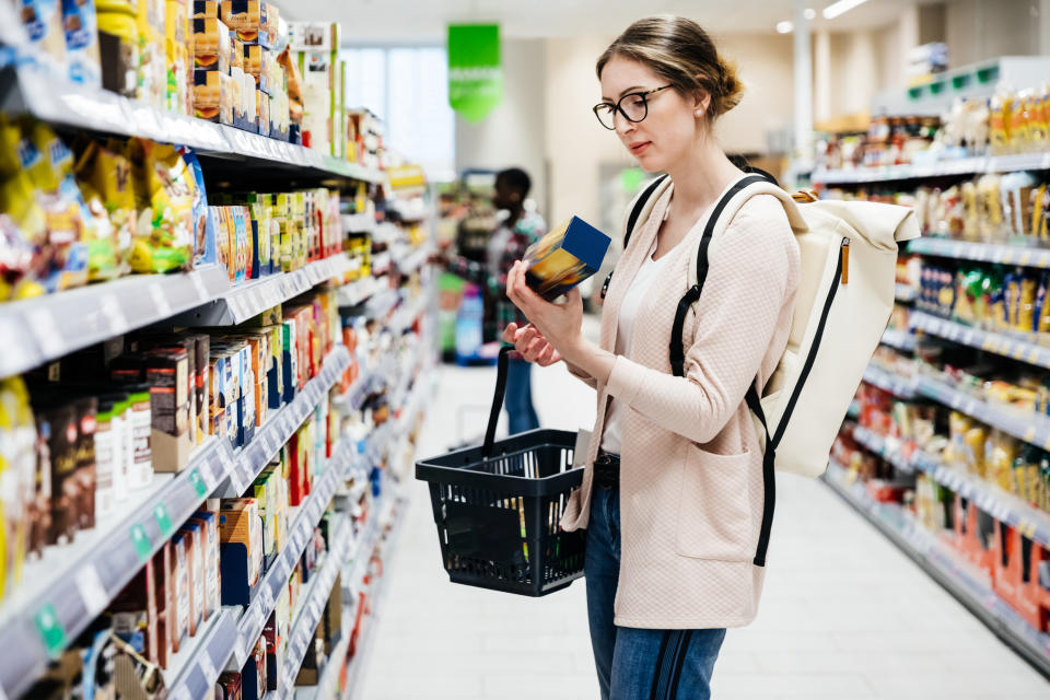 A woman reading the label on a food item while out shopping for groceries in her local supermarket.