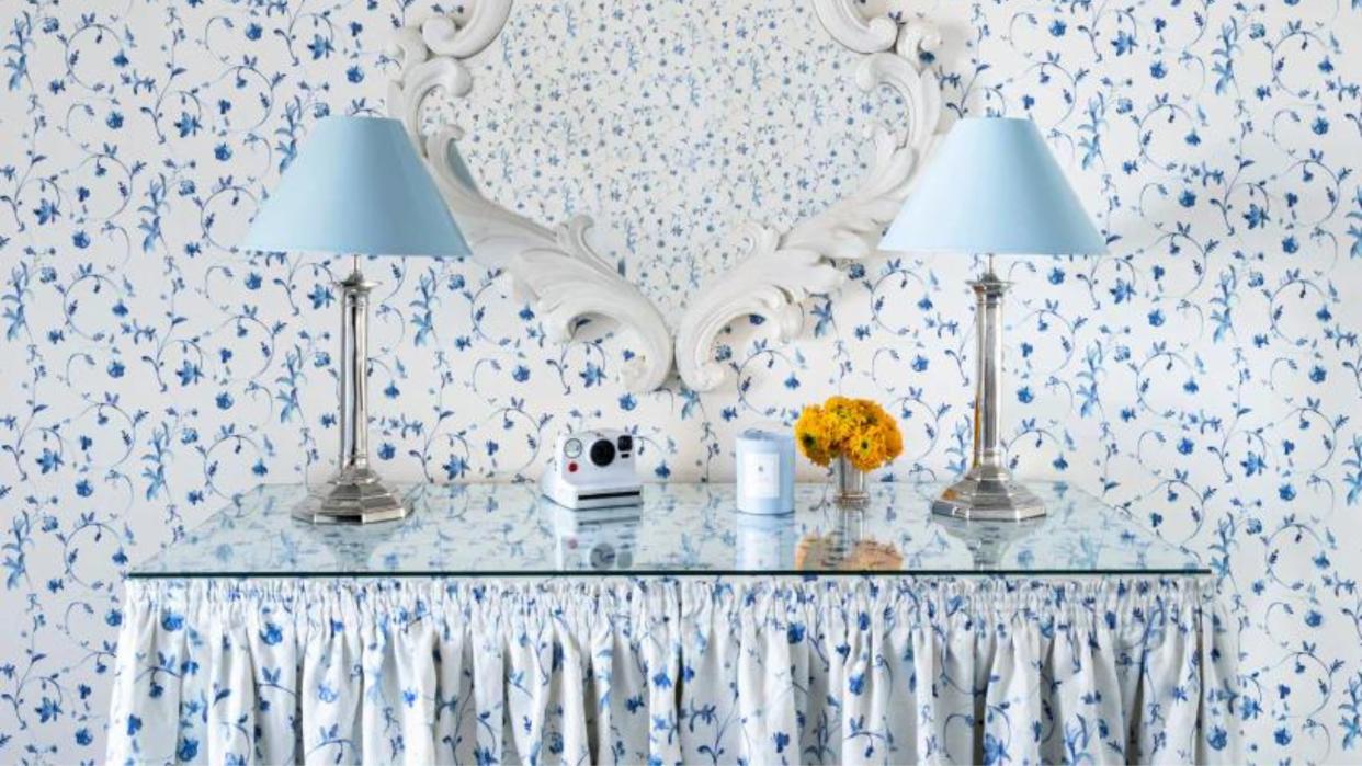  Two blue lamps on table with blue floral wallpaper. 