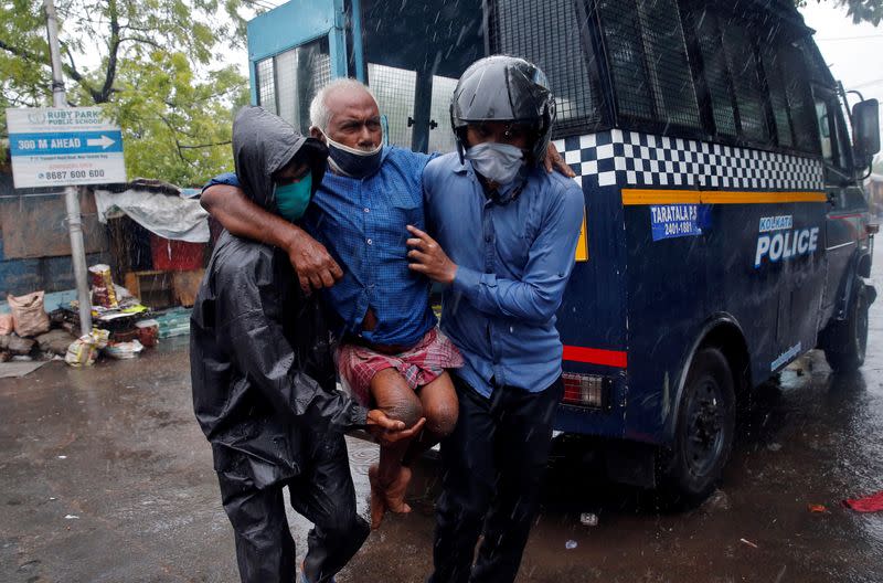 Police officers carry a disabled man to a safer place before Cyclone Amphan makes its landfall, in Kolkata