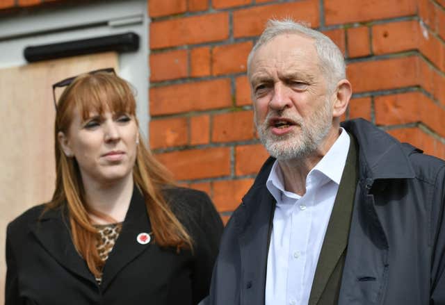 Angela Rayner and Jeremy Corbyn standing side-by-side in front of a redbrick buiilding.