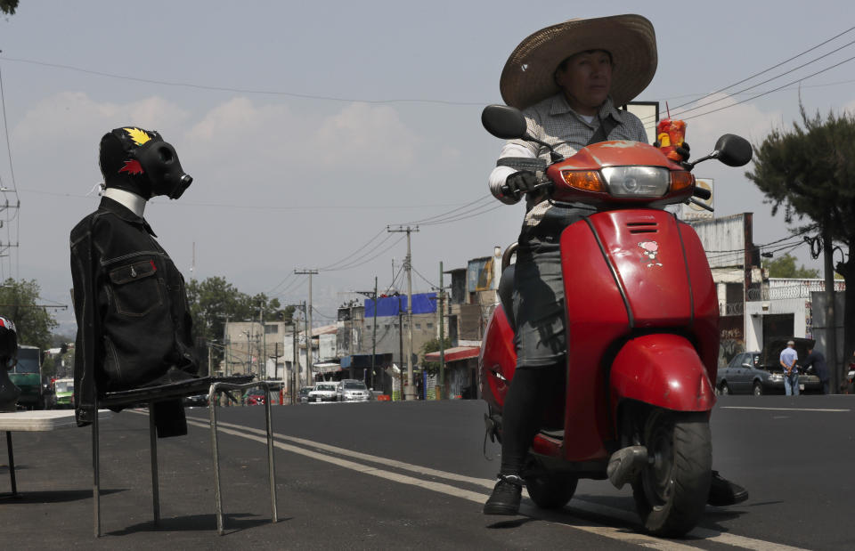 A man rides past a mannequin wearing a gas mask, a wrestling mask and a jean jacket, as a way to advertise his Mexican wrestling mask shop, in Iztapalapa, Mexico City, Thursday, April 9, 2020. The Mexico City government is sending out teams to help the home-bound and the homeless during the shutdown declared to combat the new coronavirus. (AP Photo/Marco Ugarte)