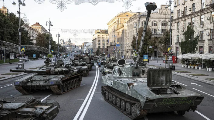 Two long lines of armored vehicles occupy a broad thoroughfare.