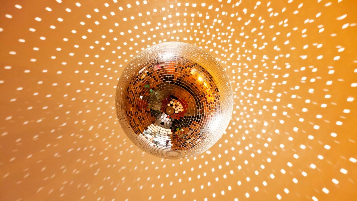  A gold-tinted disco ball reflecting light onto a gold ceiling. 