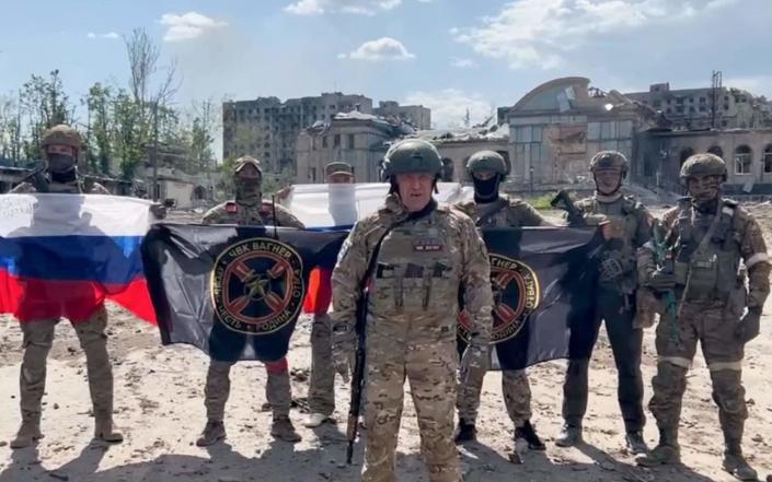 Yevgeny Prigozhin holding a Russian national flag in front of his soldiers holding Wagner Group flags in Bakhmut