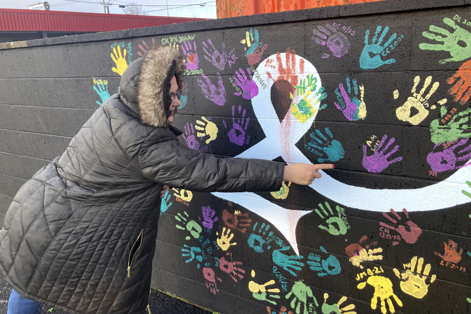 Anne Muilenburg, the office manager of Provoking Hope, an addiction recovery center in McMinnville, Ore., points to her handprint on the facility's parking lot wall on Thursday, Dec. 9, 2021. The wall has handprints of recovering addicts and the dates they became "clean." McMinnville and thousands of other towns across the United States that were wracked by the opioid crisis are on the precipice of receiving billions of dollars in the second-biggest legal settlement in U.S. history. (AP Photo/Andrew Selsky)