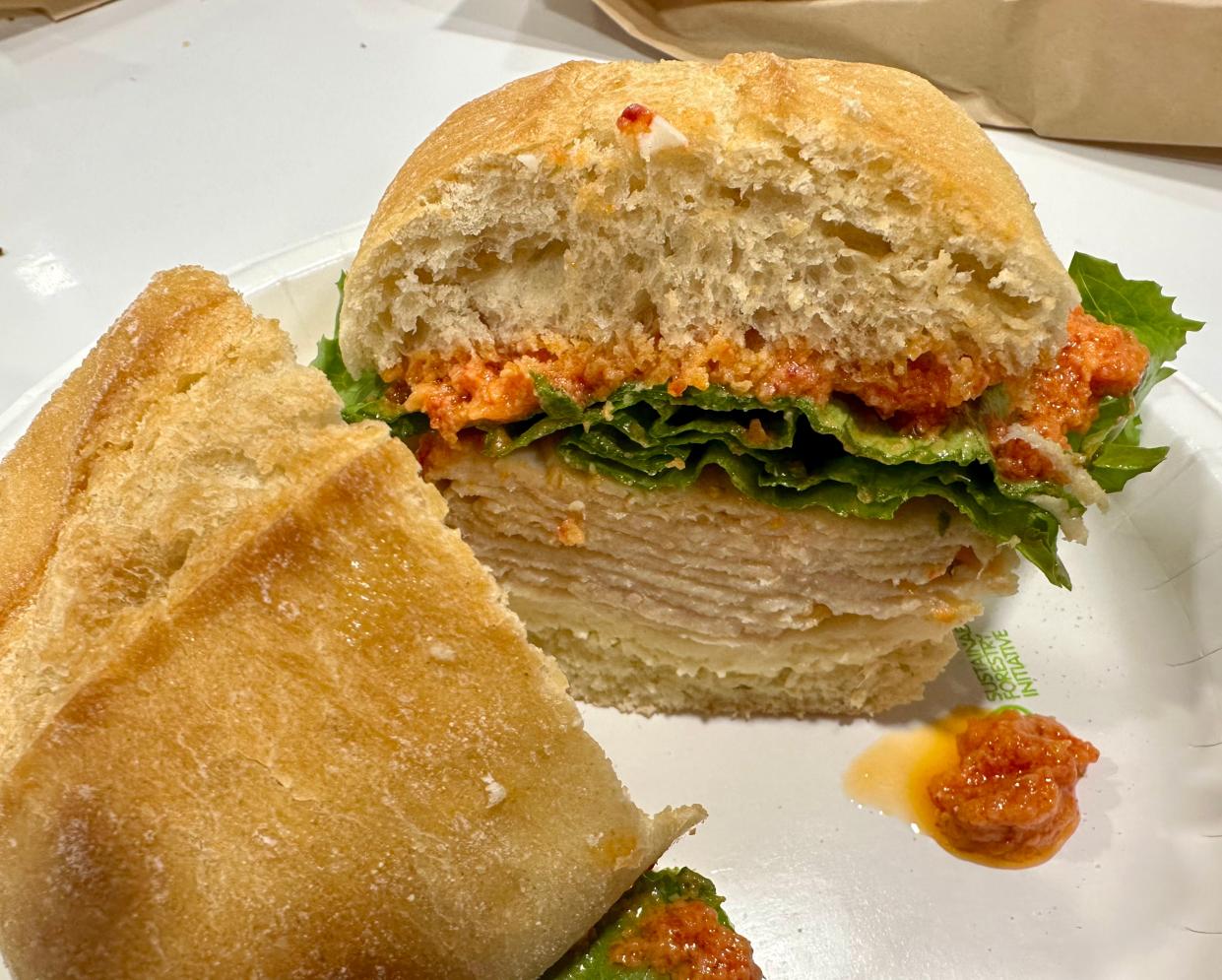 A stacked turkey breast and swiss sandwich with lettuce and a sun-dried tomato spread is served cold on a ciabatta roll at Costco food court.