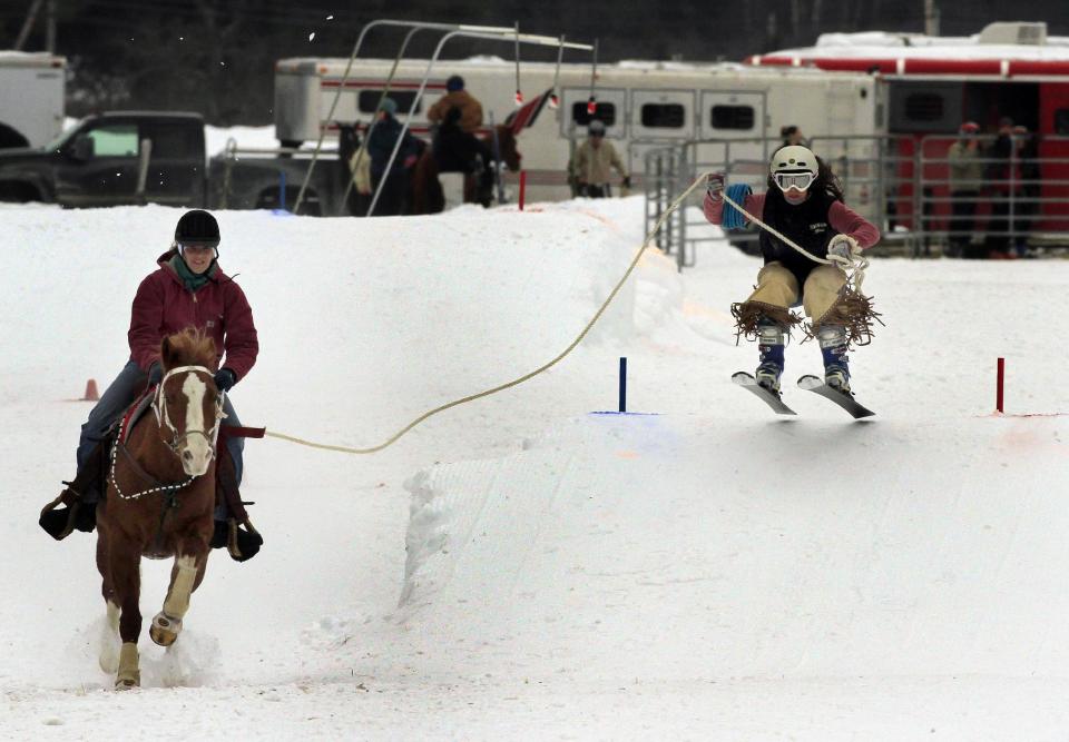 FILE - This Feb. 13, 2011 file photo shows Skier Blair Weathers of Wilmot, N.H., flying off a jump as he is pulled by Summertime and rider Jennifer Elliot during the Skijoring competition at the Newport Winter Carnival in Newport, N.H. Skijoring is a sport in which a skier is pulled over snow or ice, generally by a horse. Visitors to winter recreation destinations enjoy activities like airboarding, snowkiting and skijoring as alternatives to more traditional snow sports such as skiing or snowboarding. (AP Photo/Jim Cole, file)