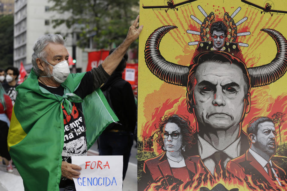 A demonstrator poses for a photo next to a banner depicting Brazilian President Jair Bolsonaro during a protest demanding Bolsonaro resign, in Sao Paulo, Brazil, Saturday, July 3, 2021. Activists called for nationwide demonstrations against Bolsonaro, gathering protestors to demand his impeachment amid allegations of potential corruption in the Health Ministry’s purchase of COVID-19 vaccines. (AP Photo/Nelson Antoine)