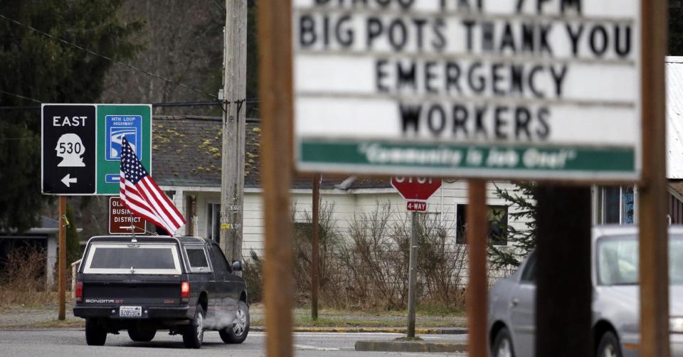 A pickup truck flying a flag drives past a sign thanking emergency workers Tuesday, March 25, 2014, in Darrington, Wash. At least 14 people were killed in a 1-square-mile slide that hit in a rural area about 55 miles northeast of Seattle on Saturday. Several people also were critically injured, and homes were destroyed. (AP Photo/Elaine Thompson)