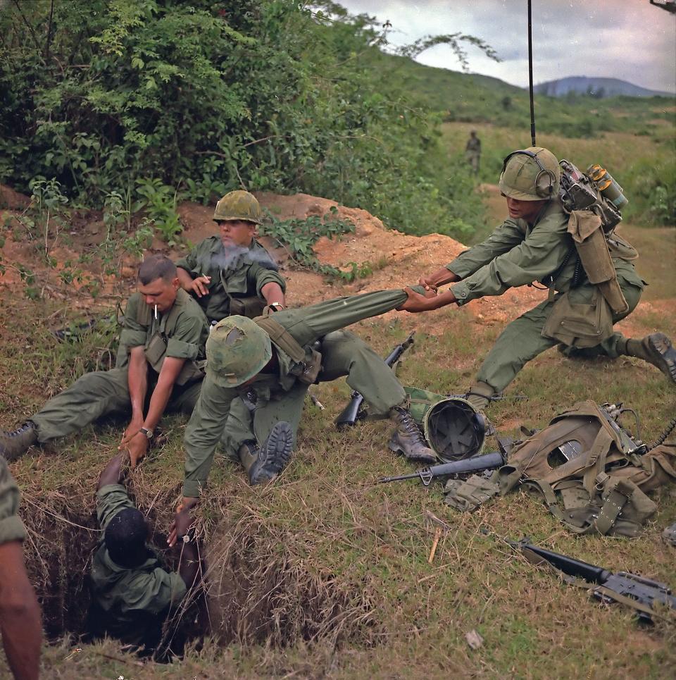 A photo of a group of soldiers lifting a man from a hole in the ground.