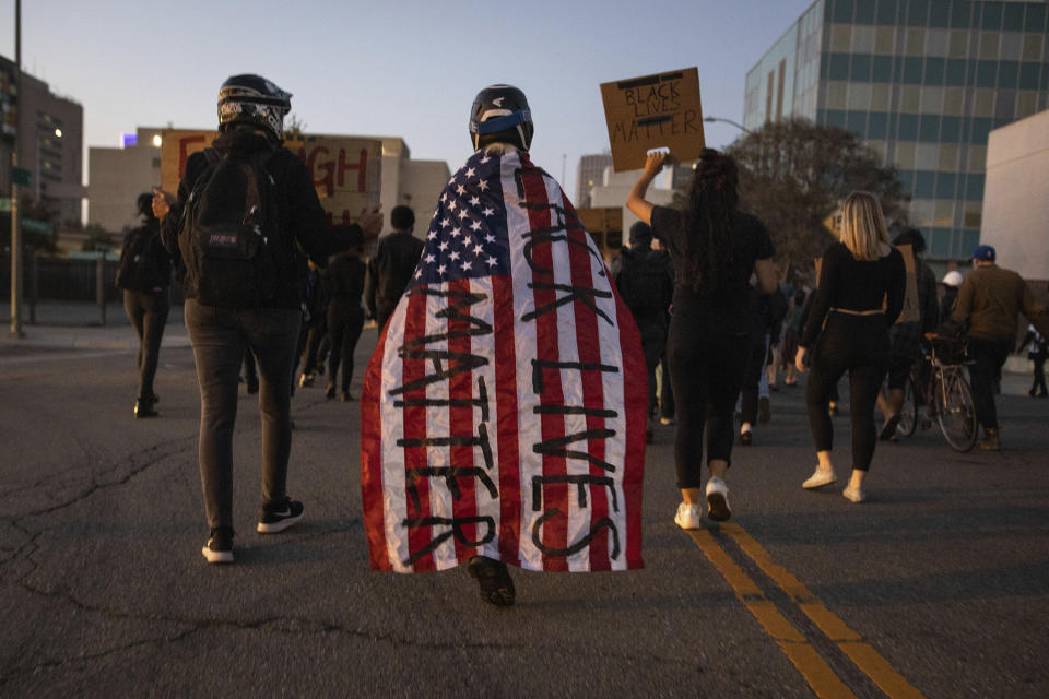 A protester wrapped in an American flag spray painted with "Black Lives Matter" marches down a street during a protest on Saturday, July 25, 2020, in Oakland, Calif. Protesters in California set fire to a courthouse, damaged a police station and assaulted officers after a peaceful demonstration intensified late Saturday, Oakland police said. (AP Photo/Christian Monterrosa)