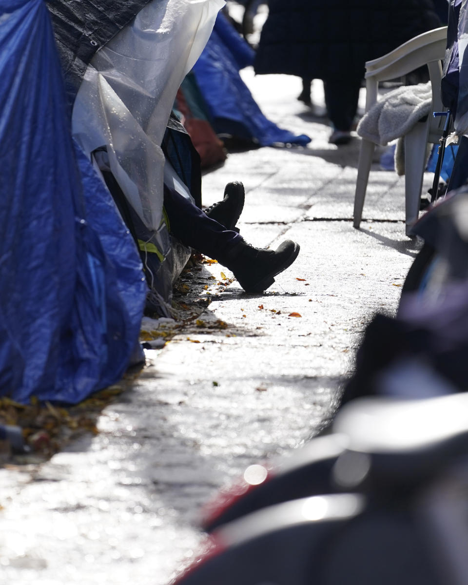 A man stretches his legs and feet outside his tent in a small migrant community, Wednesday, Nov. 1, 2023, near Northside police station in Chicago. (AP Photo/Charles Rex Arbogast)