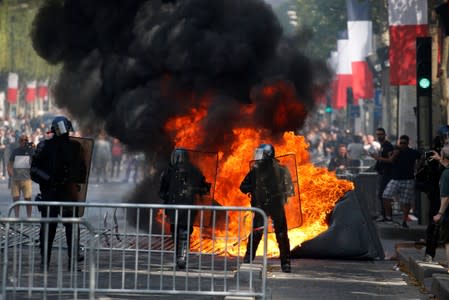 A portable toilet burns next to French Gendarmes during clashes with protesters on the Champs Elysees avenue after the traditional Bastille Day military parade in Paris