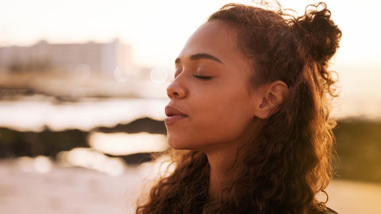 shot of an attractive young woman sitting alone on a mat and meditating on the beach at sunset