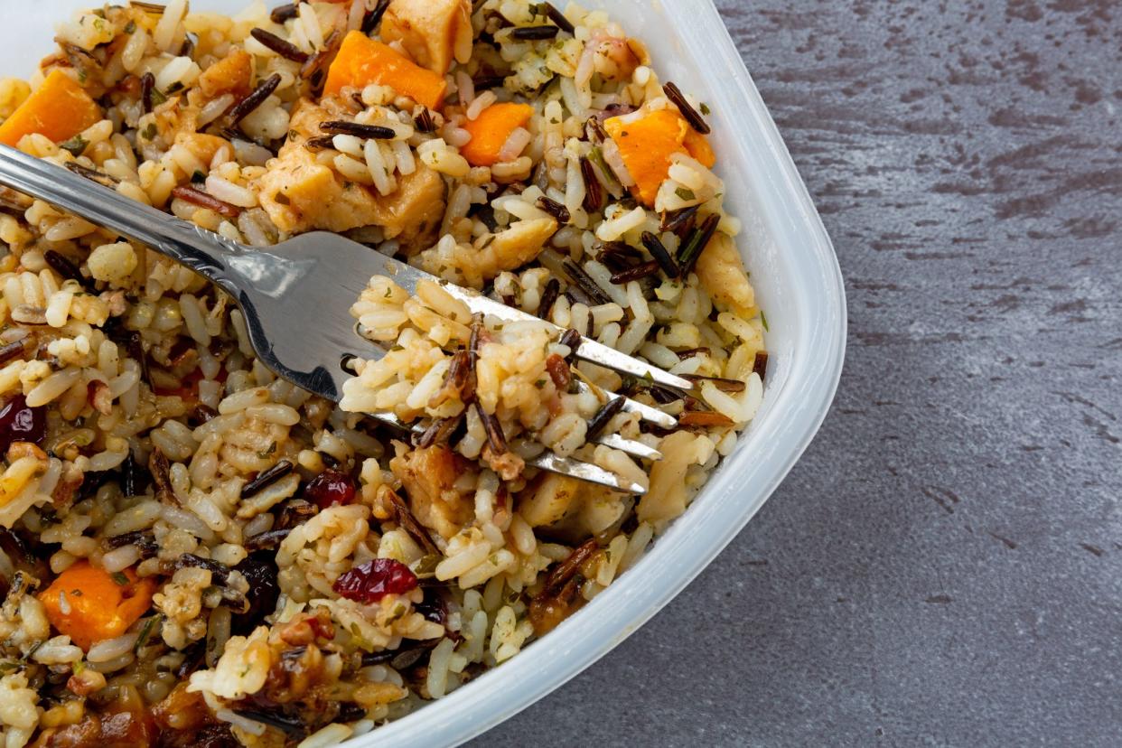 Close view of a chicken with pecans and wild rice TV dinner in a plastic tray with a fork on the food atop a gray background illuminated with natural lighting.