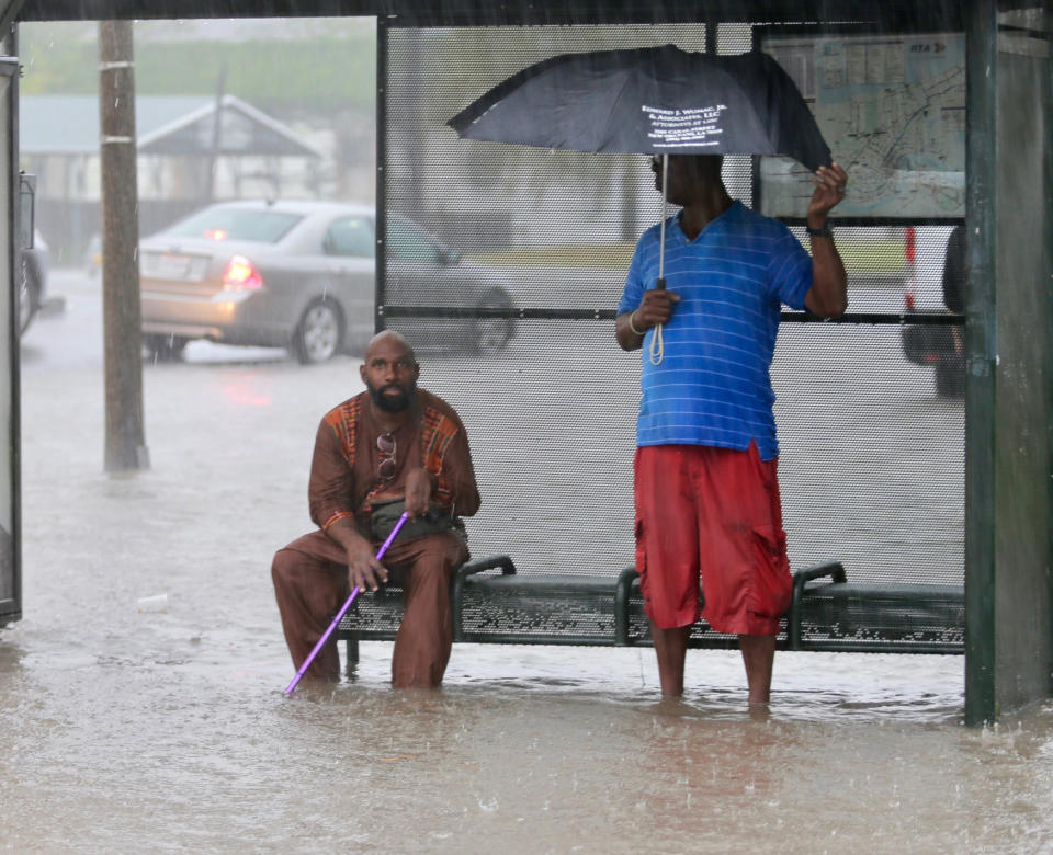 Residents sit under a bus shelter along a flooded Broad Street as heavy rain falls, Wednesday, July 10, 2019, in New Orleans. (David Grunfeld/The Advocate via AP)