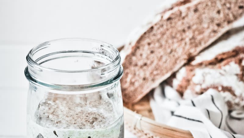 Sourdough starter in a jar with bread behind it.