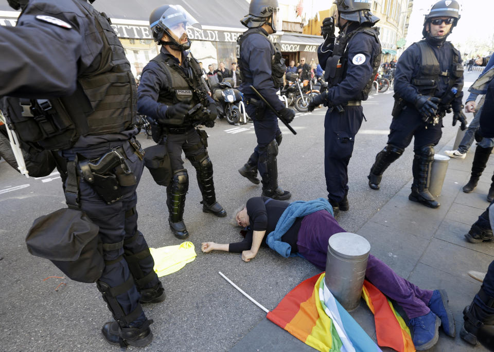 FILE - In this Saturday, March 23, 2019 file picture, anti-globalization activist Genevieve Legay, 73, lies unconscious after collapsing on the ground during a protest in Nice, southeastern France, as part of the 19th round of the yellow vests movement. Genevieve Legay was waving a rainbow flag marked "Peace" and a yellow vest when riot police carrying shields suddenly pushed toward the group of a few dozen protesters Saturday. (AP Photo/Claude Paris, File)