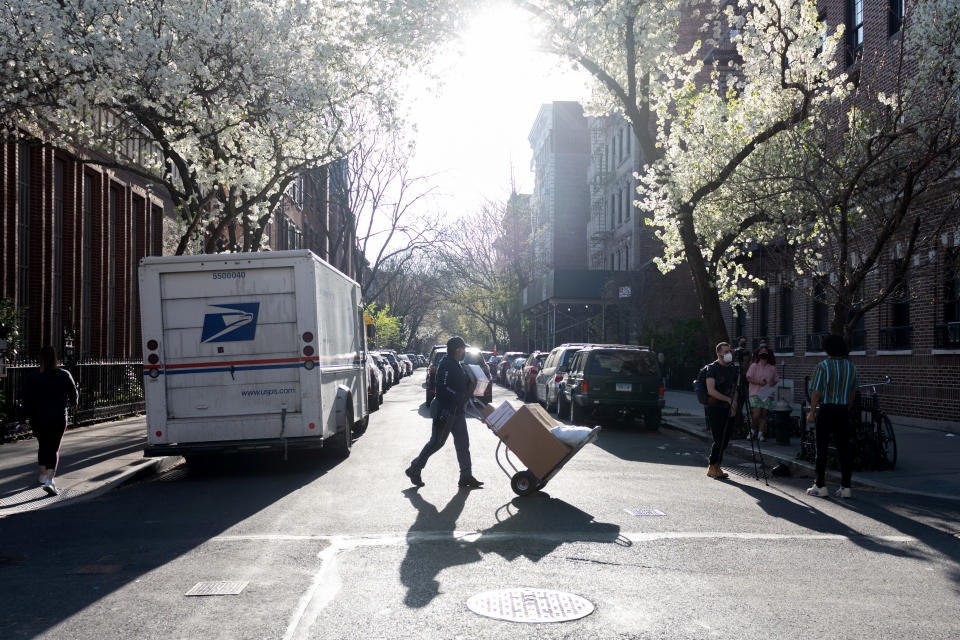 A USPS mail worker casts a shadow while wheeling boxes near Japanese Cherry Blossom trees  in the West village amid the coronavirus pandemic on April 07, 2021 in New York City. (Alexi Rosenfeld/Getty Images)