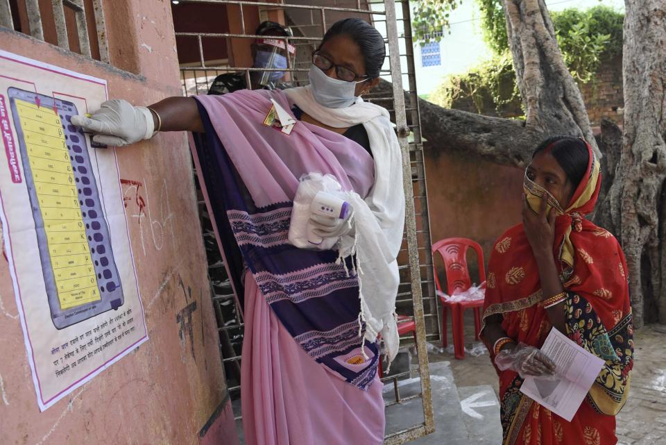 A woman explains the working of an electronic voting machine (EVM) to a voter at a polling station, during the first phase of state elections at Paliganj, in the eastern Indian state of Bihar, Wednesday, Oct. 28, 2020. With an overall declining coronavirus positive trend, Indian authorities decided to hold the first state legislature election since the outbreak of COVID-19. People began voting Wednesday in the country’s third largest state Bihar with of a population of about 122 million people. (AP Photo/Aftab Alam Siddiqui)