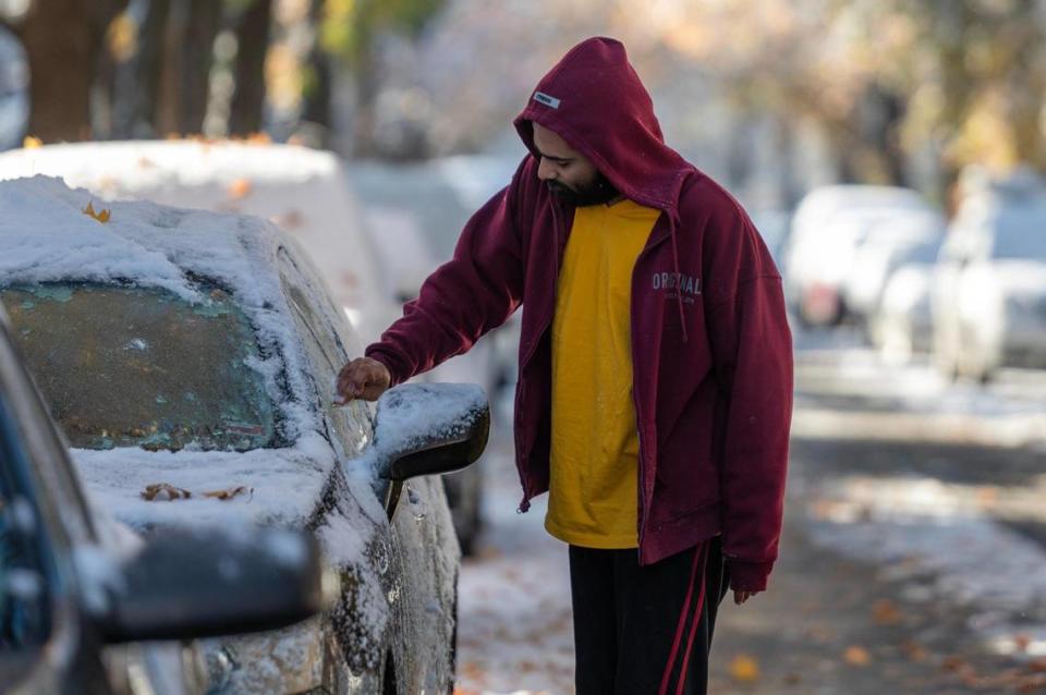 A commuter uses a plastic card to scrape ice off their car window following Kansas City’s first snowfall of the season on Sunday, Nov. 26, 2023.