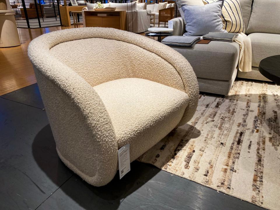 A white accent swivel chair with boucle fabric on the floor at Crate and Barrel next to a cream-colored rug