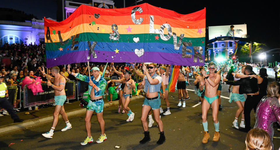 Four men can be seen holding a large rainbow flag on sticks as they walk in the Mardi Gras parade along Oxford Street.