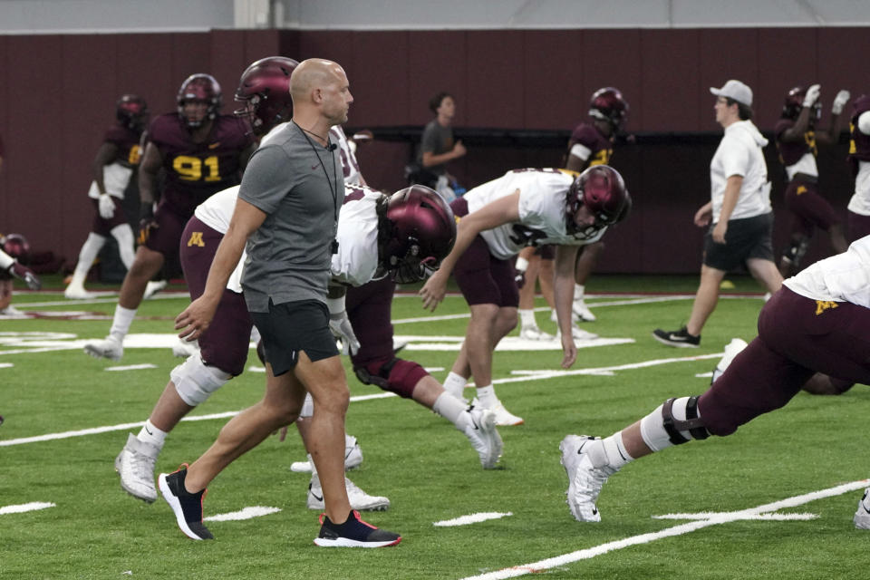 FILE - University of Minnesota head coach P.J. Fleck, left, walks amongst his players during stretching drills at the team's NCAA college football practice in Minneapolis, Saturday, Aug. 6, 2022. Fleck has called them the "Encore Four," a group of super seniors once again taking advantage of the pandemic-prompted extra eligibility to play one more year for the program they've helped elevate and grown to love. (AP Photo/Jim Mone, File)