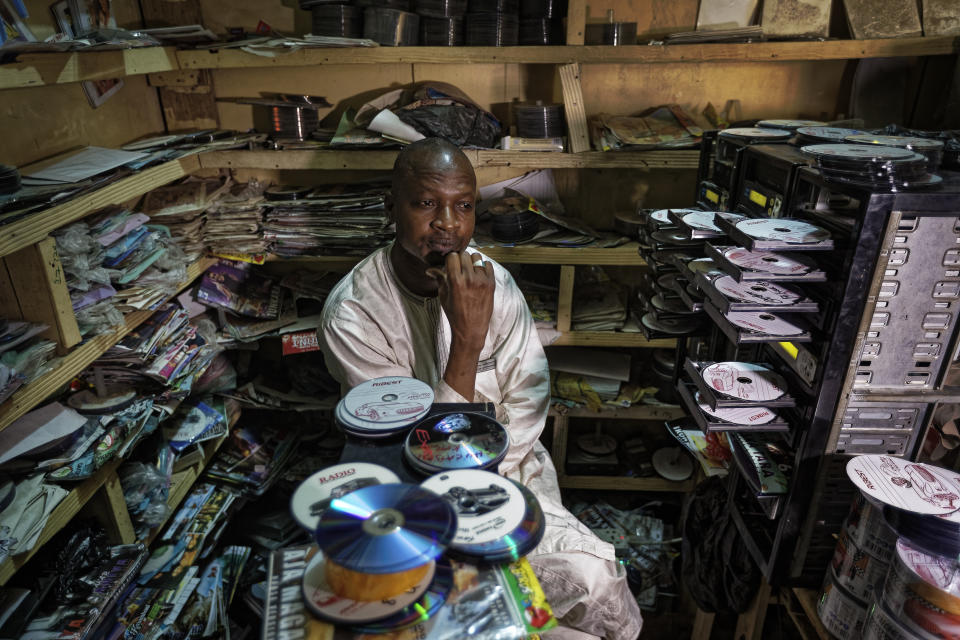 In this photo taken Tuesday, Feb. 19, 2019, Hassan Mohammed waits for his duplicating machines to start up as he prepares to copy Hausa-language DVDs to sell in the market in Kano, northern Nigeria. Faced with an election that could spiral into violence, some in the popular Hausa-language film industry known as Kannywood assembled this week to shoot an urgent music video appealing to the country for peace. (AP Photo/Ben Curtis)