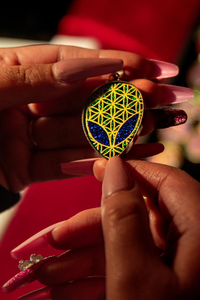 Hands hold a sacred geometry pendant in the shape of an alien head