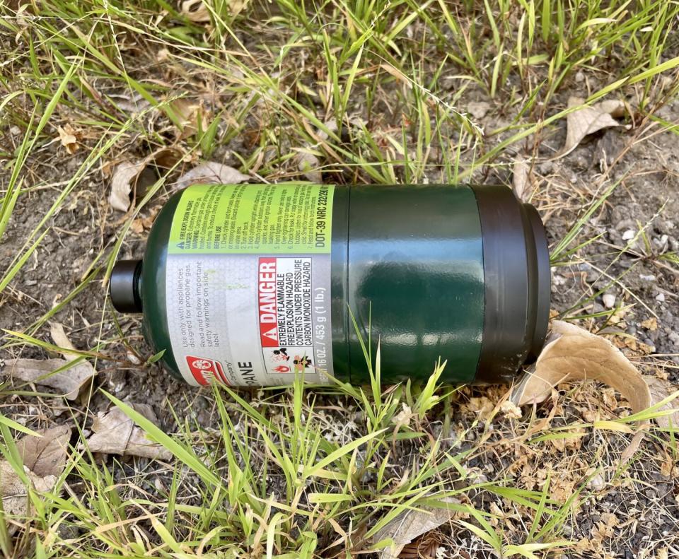 A propane cannister lies on the ground.