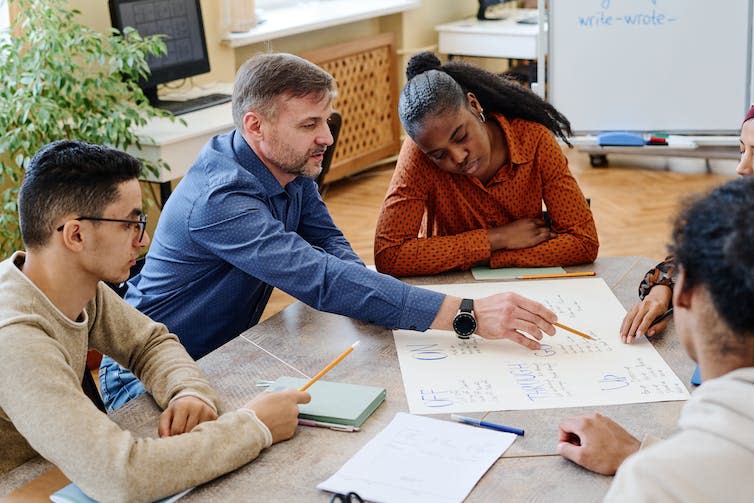 A group of adults sit around a table looking at an A3 piece of paper.