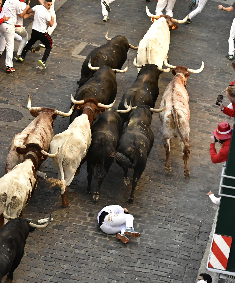 A runner falls as people run through the street with fighting bulls at the San Fermin Festival in Pamplona, northern Spain, Friday, July 8, 2022. Revellers from around the world flock to the city every year for nine days of uninterrupted partying in Pamplona's famed running of the bulls festival which was suspended for the past two years because of the coronavirus pandemic. (AP Photo/Alvaro Barrientos)