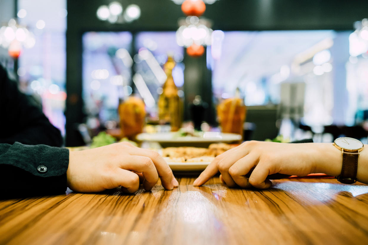 Two hands almost touch across restaurant table in coronavirus age