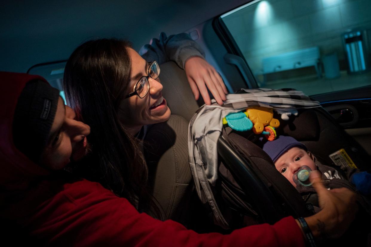 Two adults lean over a toddler in a carseat.