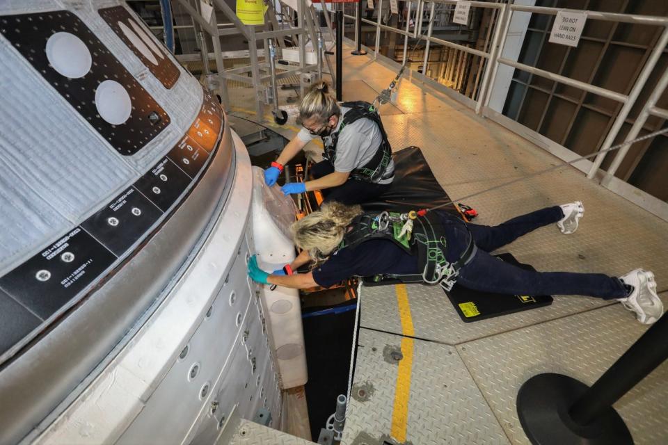 two engineers wearing harnesses with bungee lines work on starliner spaceship atop rocket