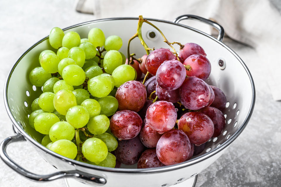 Two varieties of grapes, red and green in a colander. Gray background. Top view.