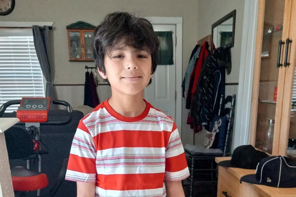 A little boy in a red-and-white striped shirt, standing inside a home