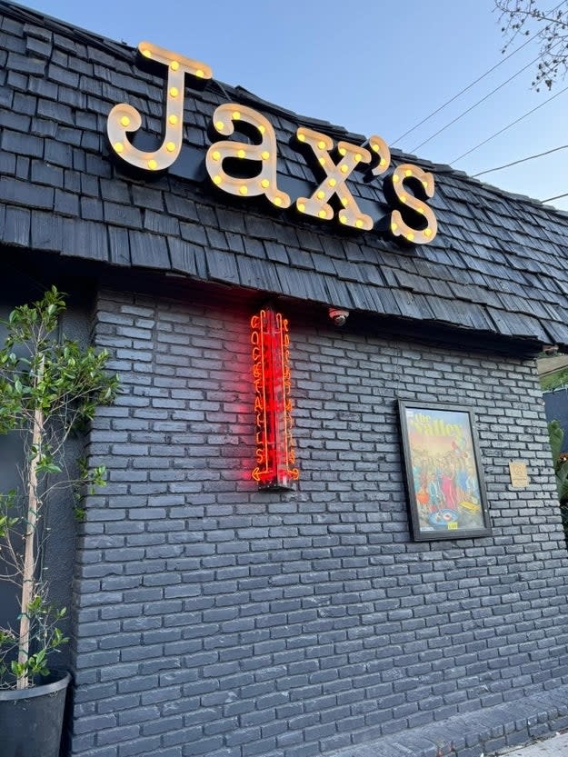 Exterior of Jax's restaurant with lit signage and neon light, next to a framed picture on the wall