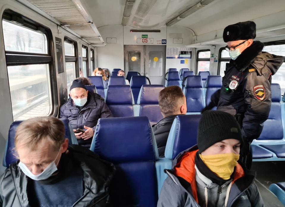 A Russian police officer checks public adherence of the 'mask regime' forcing people to wear masks in public places, in an electric train car in Moscow, Russia, Friday, Nov. 27, 2020. Russia has registered a sharp spike in coronavirus cases Friday, with officials reporting 27,543 new confirmed infections, which is over 2,000 contagions more than the day before and the highest in the pandemic. (Denis Voronin, Moscow News Agency photo via AP)