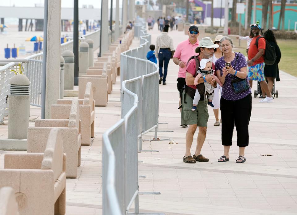Visitors stroll past metal barricades earlier this month along the Daytona Beach Boardwalk blocking access to the beach due to damage from tropical storms Ian and Nicole.