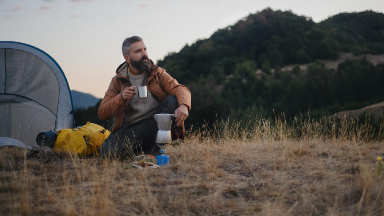  Man sitting in the wilderness outside his tent drinking a hot drink. 