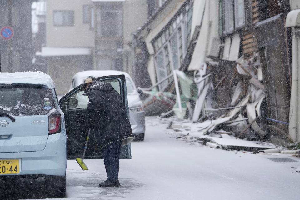 A person cleans his car from snow in Wajima in the Noto peninsula facing the Sea of Japan, northwest of Tokyo, Sunday, Jan. 7, 2024. Monday's temblor decimated houses, twisted and scarred roads and scattered boats like toys in the waters, and prompted tsunami warnings. (AP Photo/Hiro Komae)