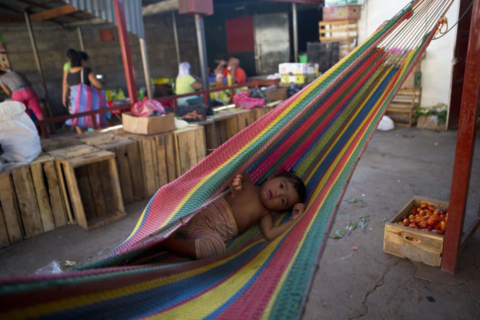In this Aug. 18, 2018 photo, one-year-old Sofia Camila rocks in a hammock as her mother Marisol Alvarez tries to put her down for a nap while selling fruit and vegetables inside the market in Intipuca, El Salvador. Former residents now in the U.S. support Intipuca, even paying for teachers at the local public school, making sure children learn English. (AP Photo/Rebecca Blackwell)