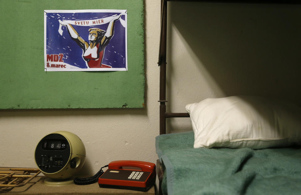 Phone and clock stand next to a bed as part of an installation at the nuclear shelter from Cold War era at five star Jalta Hotel in downtown Prague, Czech Republic, Wednesday, Dec. 4, 2013. To mark the 55th anniversary, the hotel began to turn the bunker into an Iron Curtain museum whose first part was opened to the public, Nov. 2013. Slogan on the poster means "World Peace". (AP Photo/Petr David Josek)