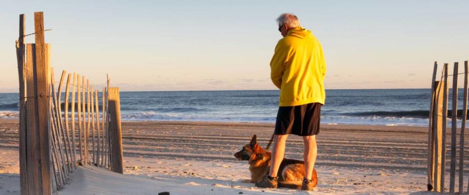 Senior man with dog enjoying a morning on a sandy beach in the Outer Banks of North Carolina.