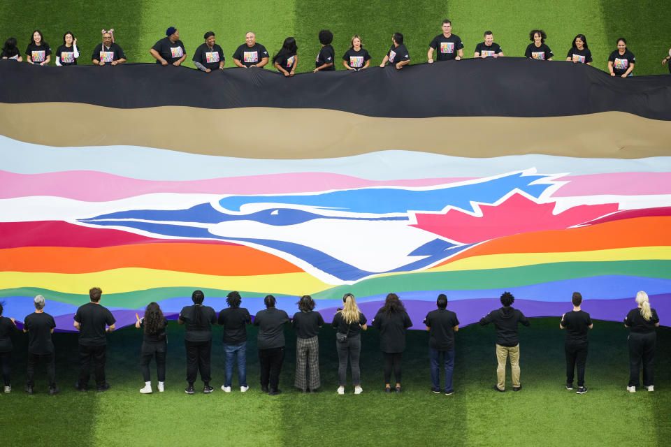 People hold a Pride-themed Toronto Blue Jays flag to celebrate Pride Weekend before the team's baseball game against the Minnesota Twins on Friday, June 9, 2023, in Toronto. (Mark Blinch/The Canadian Press via AP)