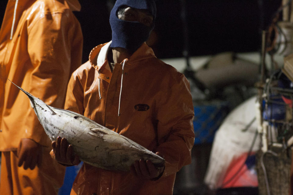 FILE - In this March 23, 2016 file photo, a foreign worker unloads fish from a U.S. fishing vessel at Pier 38 in Honolulu. On Friday, Sept. 18, 2020 the Hawaii Supreme Court heard arguments on the legality of issuing licenses to foreign workers in Hawaii's longline commercial fishing fleet, which for years has been under scrutiny after an Associated Press investigation revealed claims of human trafficking and questionable labor practices.(AP Photo/Caleb Jones, File)