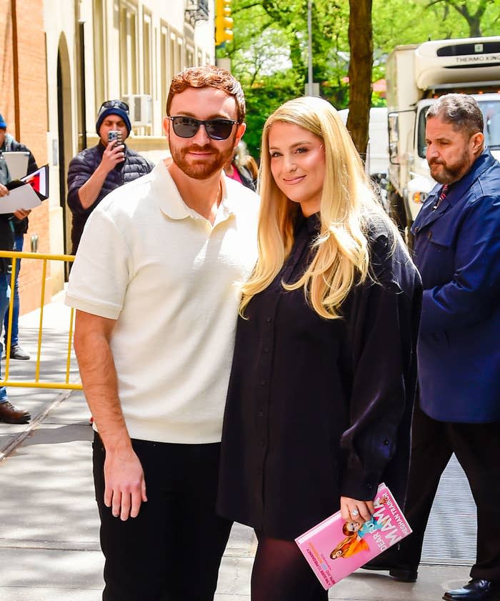 megan and her husband posing on a sidewalk as she holds her book